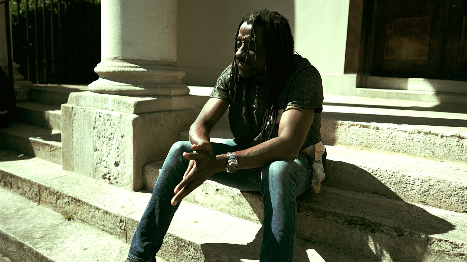 South London rapper Airklipz sitting on a staircase of an old building.